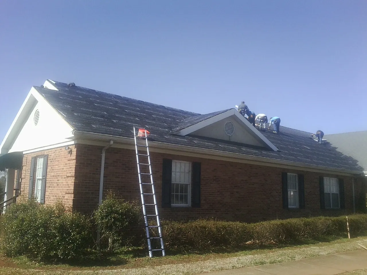 Crew tearing shingles off a brick ranch roof with a ladder set — Metal Roof Repair work by our crew in Perham