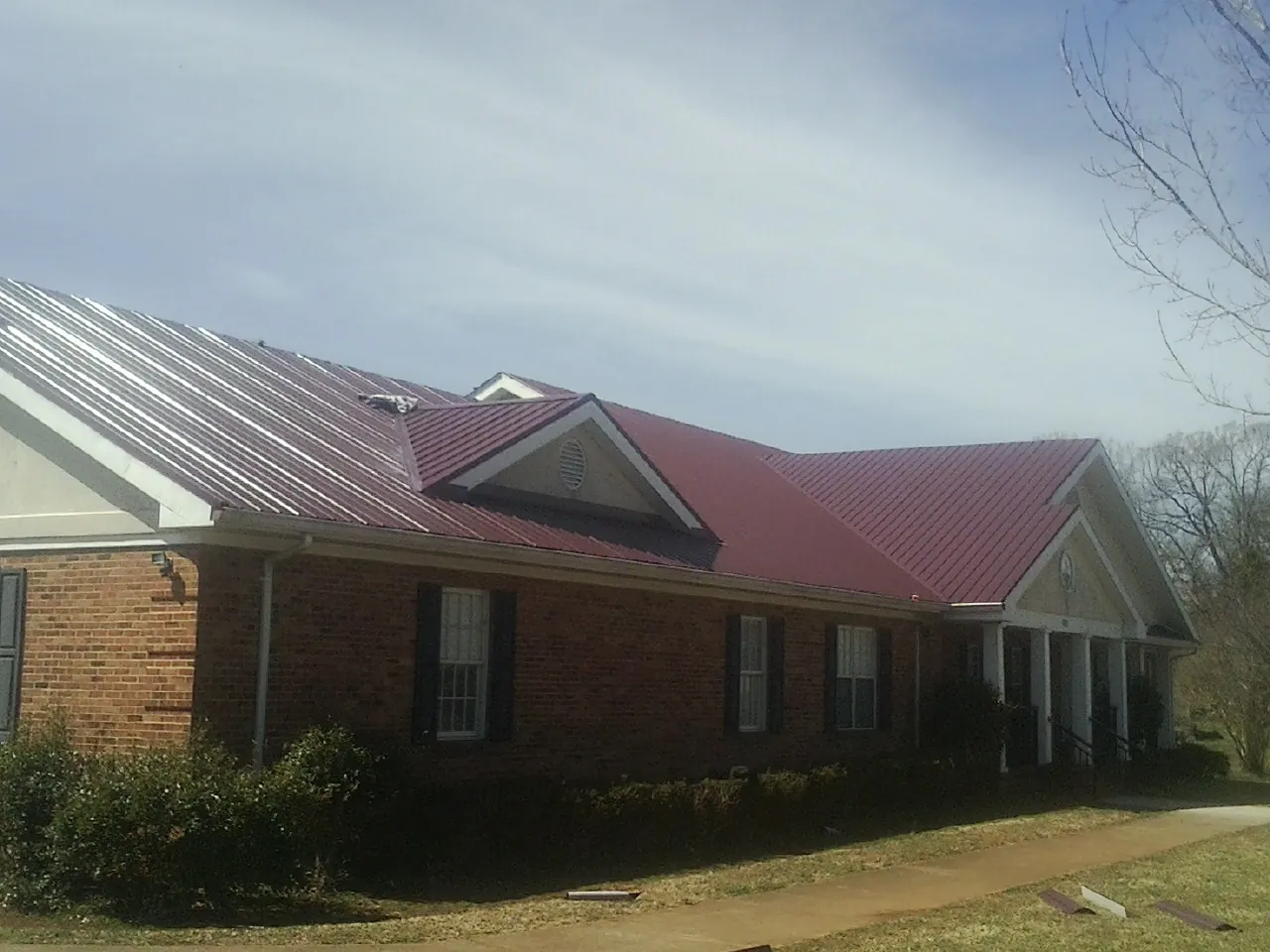 Red metal roof with gabled entries on a long brick building, from a Hail Damage Roof Repair job in Perham