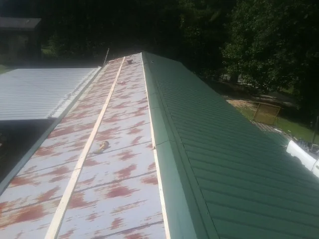 Old rusted panels beside newly installed green metal roofing — Wind Damage Roof Repair by Roofing Brothers in Perham