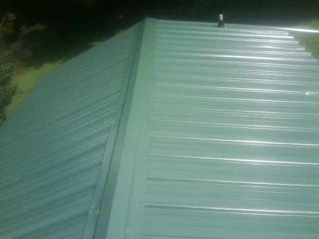 New green metal panels meeting at the ridge of a roof — Flat Roof Repair work by our crew in Perham