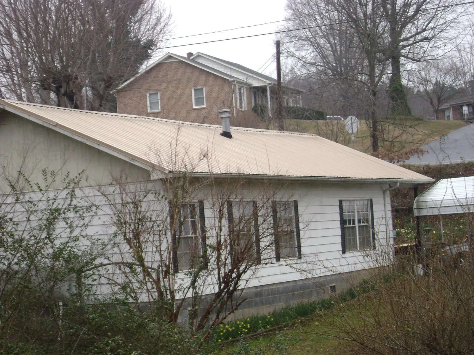 Tan metal roof on a white sided house set into a hillside — Commercial Roofing by Roofing Brothers in Perham