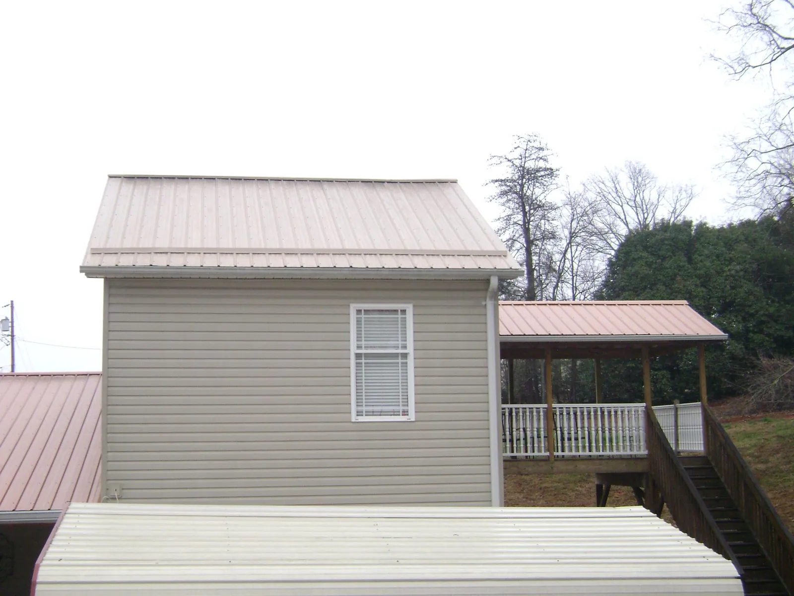 Tan metal roofs on a two story addition and attached porch, from a Roof Replacement job in Perham